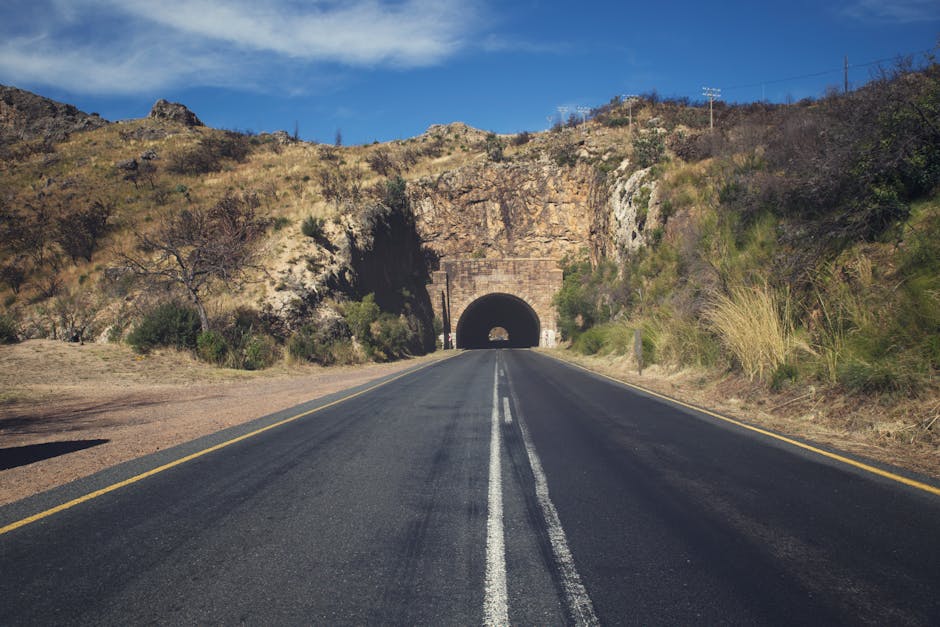Scenic mountain road leading into a tunnel under a clear blue sky.